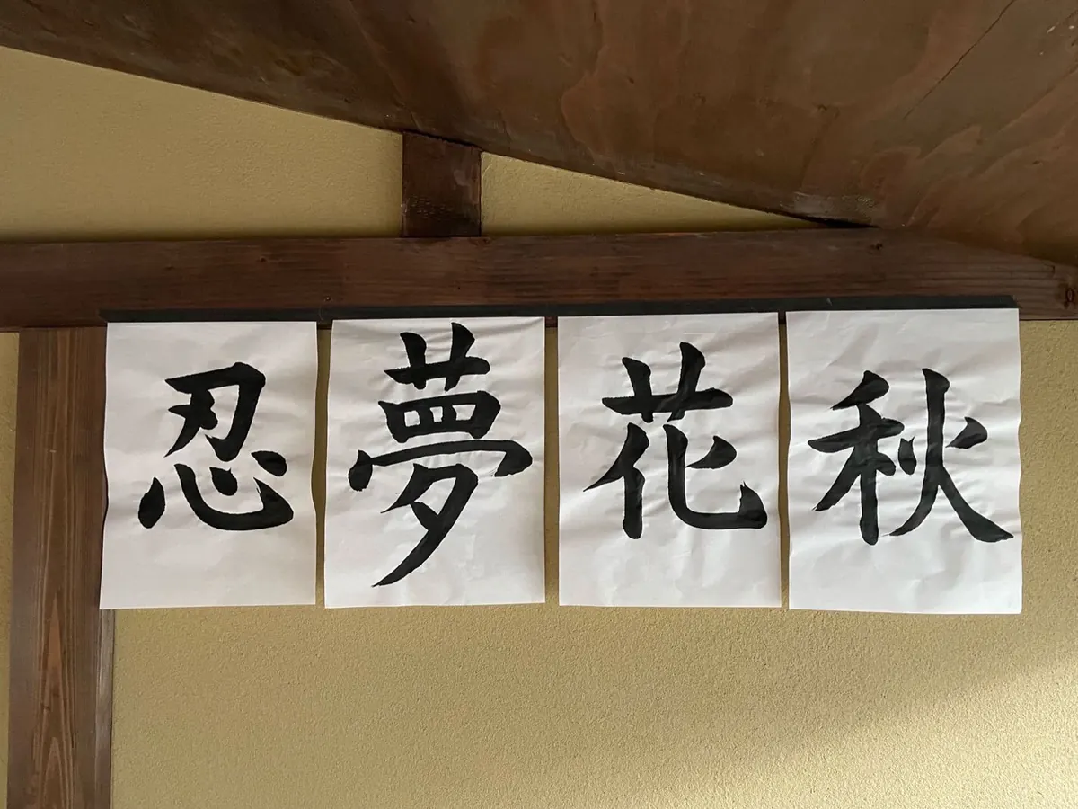 Four kanji works hanging on the wall: 忍 夢 花 秋